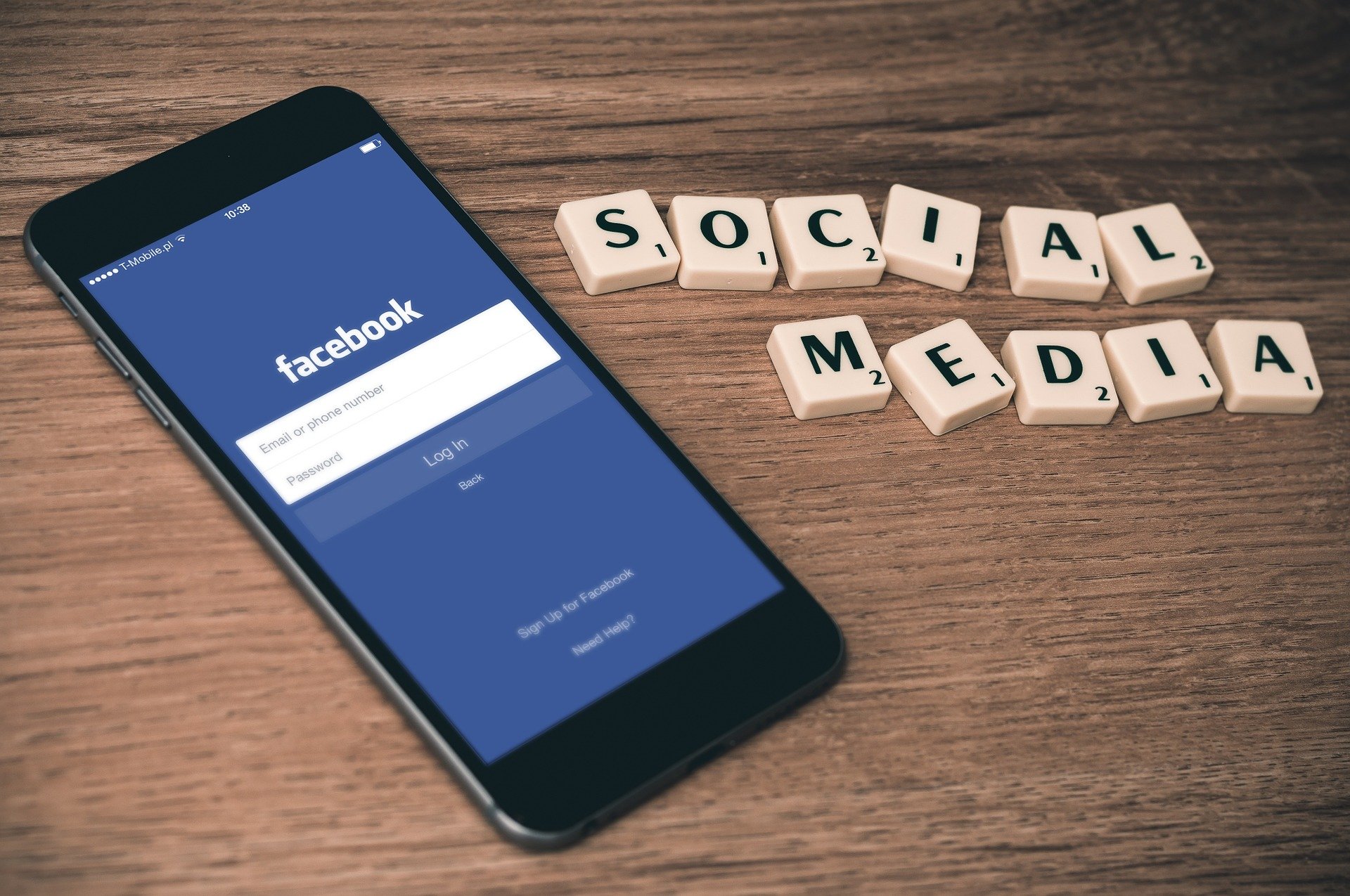 EIn Smartphone liegt auf einem Tisch. Darauf ist die Login-Seite von Facebook zu sehen. Daneben liegen Scrabble-Klötze, die das Wort